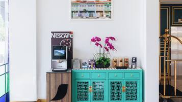 Una máquina de café Nescafé, una orquídea en maceta y un cuadro con una imagen de un edificio sobre un mueble color turquesa.