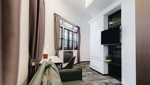 A modern hotel room with a sofa, a dining table, a TV, and a kitchen area.