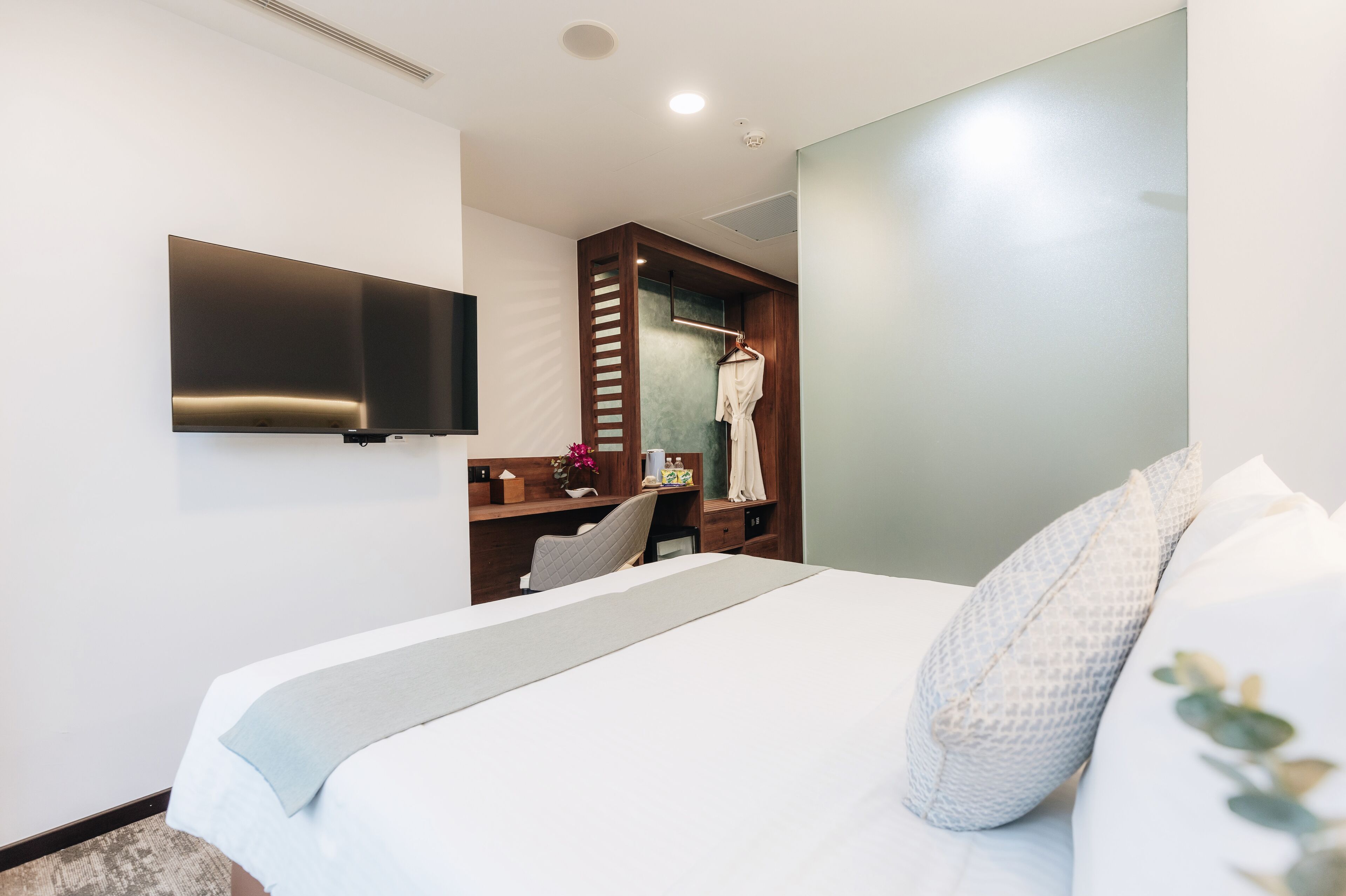 A modern hotel room with a large bed, a desk, a television, and a walk-in closet.