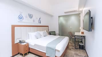 Habitación de hotel moderna con una cama grande, mesita de noche con teléfono, un escritorio con silla y una obra de arte en la pared.