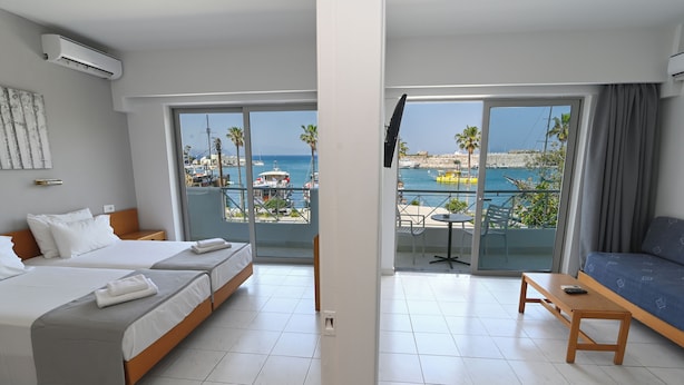 A hotel room with two beds, a balcony with a view of the sea, and a sofa. - Jasmine Hotel Apartments (Kos)