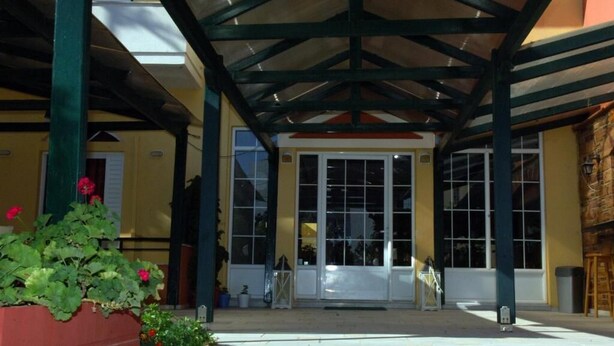 A covered entrance with a glass door, a planter with flowers, and a clear view of the interior. - Sunrise Hotel (Chios)
