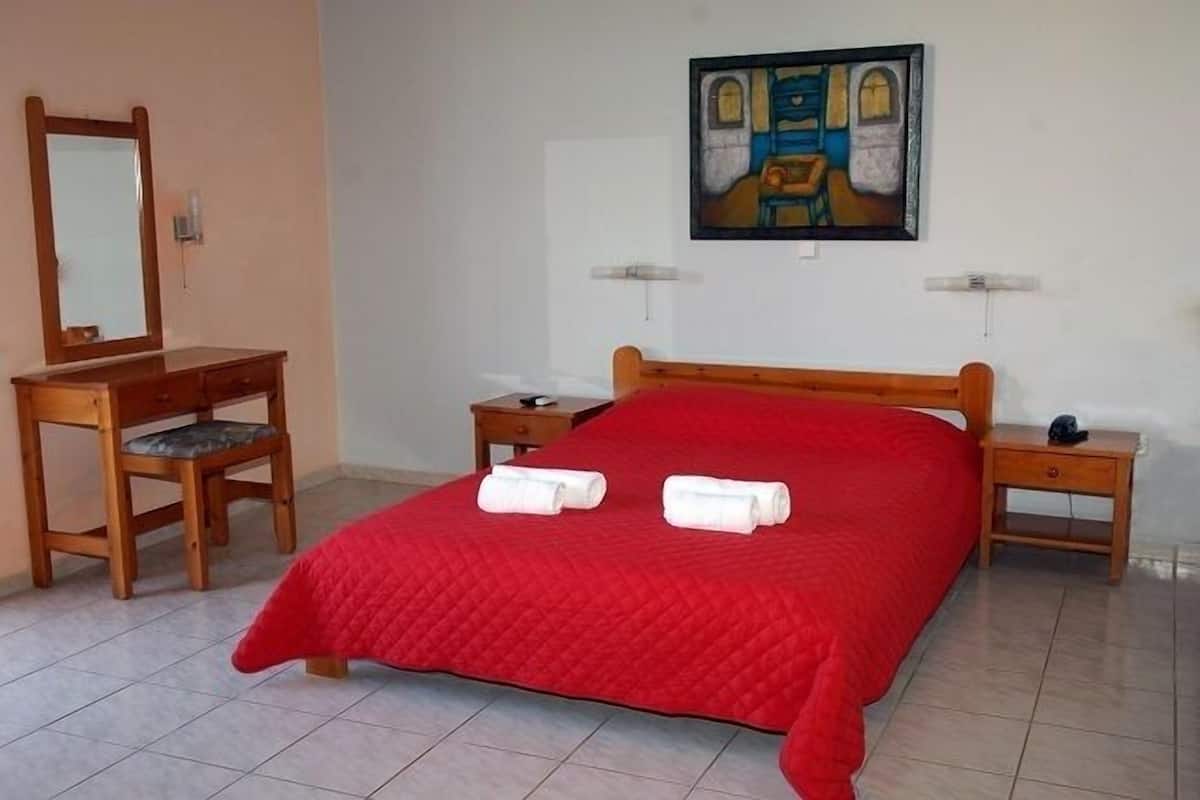 Une chambre avec un lit en bois, une commode en bois, une chaise et un tableau accroché au mur.