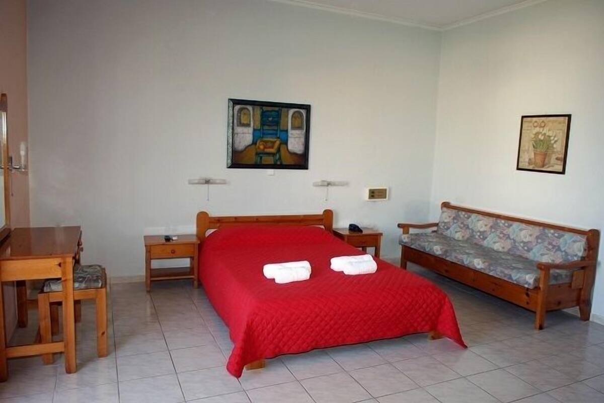 Une chambre à coucher comprenant un lit, un bureau en bois, une chaise, un canapé et deux lampes fixées au mur.