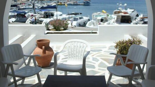 Una terrazza con sedie e tavolo bianchi, vista su una marina con barche e cielo sereno.