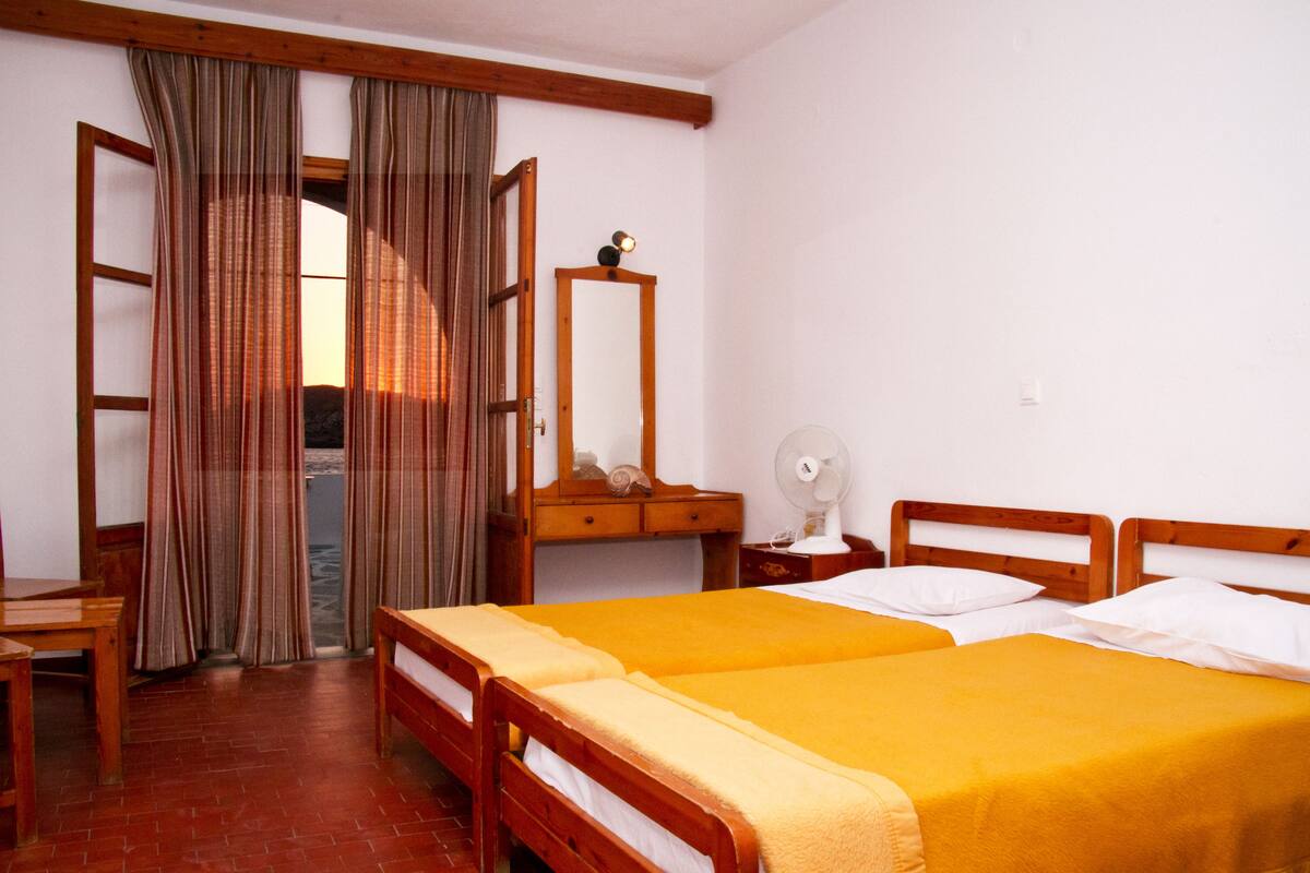 A room with two beds, a wooden dresser, a mirror, and a fan.