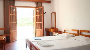 A hotel room with two beds, a wooden desk, a chair, a mirror, and a large window with curtains.