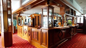 Uma área de bar com balcões de madeira, tapete com padrão vermelho e um espelho grande.