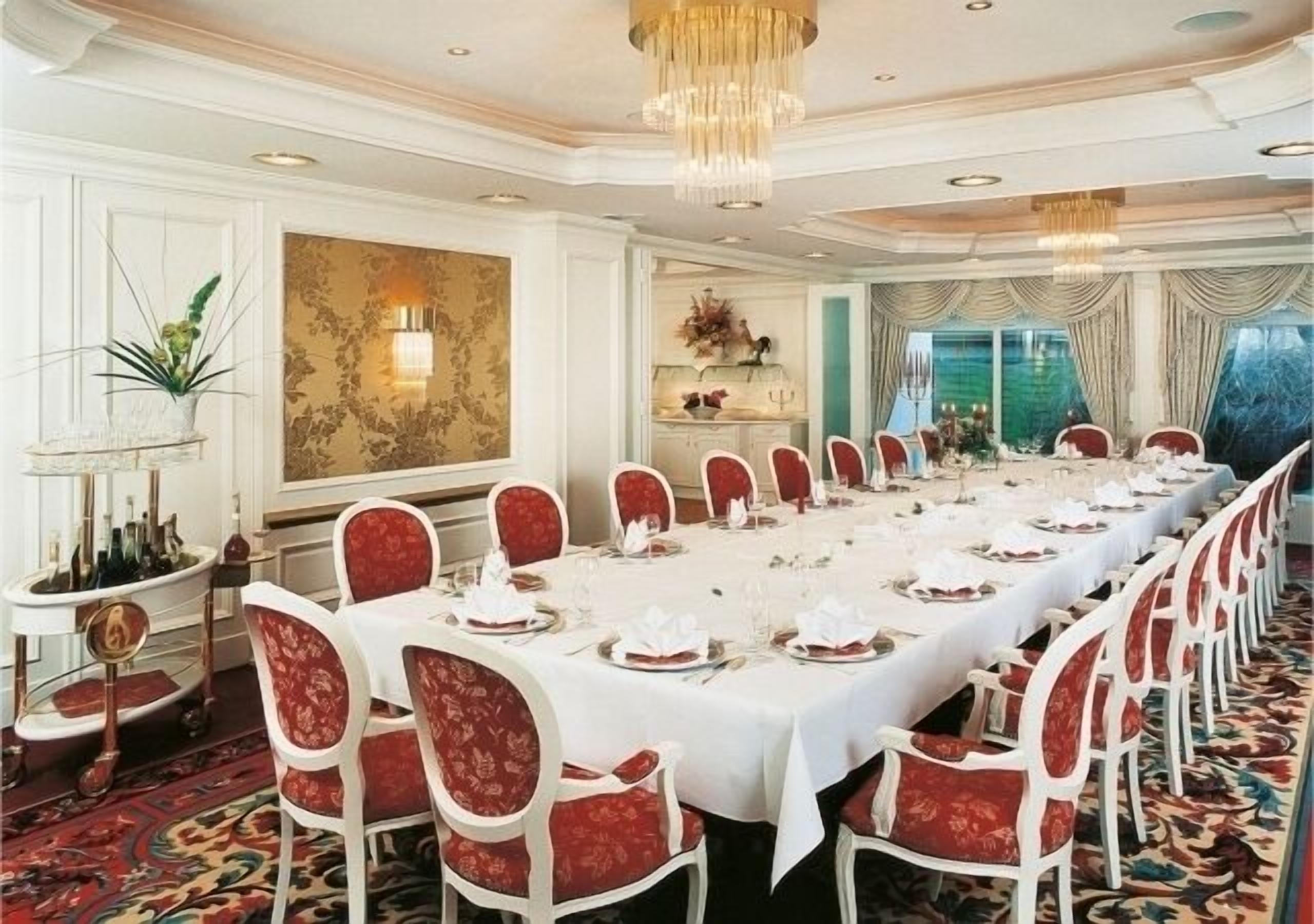 Un comedor formal con una larga mesa dispuesta para una comida, sillas tapizadas en rojo y un candelabro.