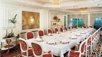 Un comedor formal con una larga mesa dispuesta para una comida, sillas tapizadas en rojo y un candelabro.