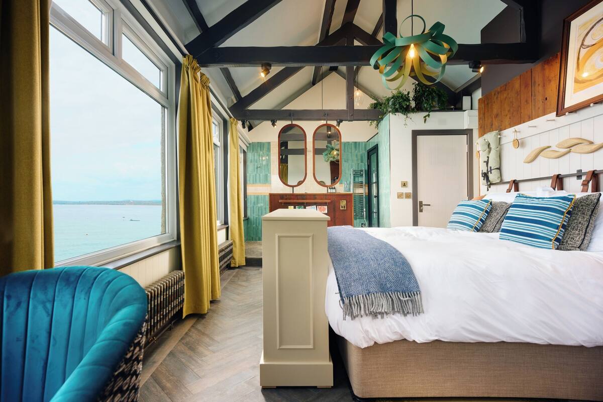 A bedroom with a large window, a bed, a chair, and a dresser.