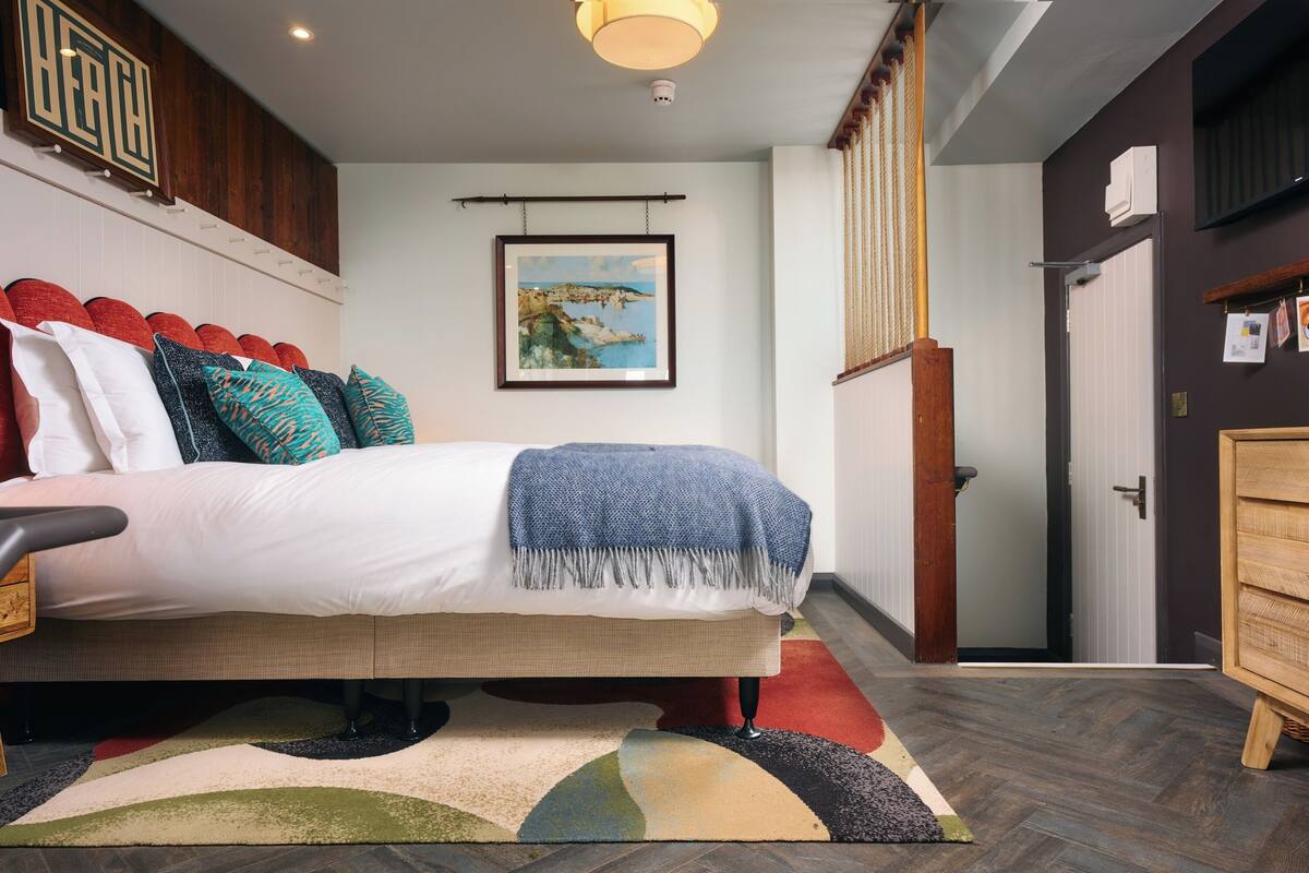 A bedroom with a bed, a wooden headboard, a framed picture on the wall, a wooden wardrobe, and a door.