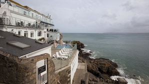 Un hotel frente al mar con piscina, sillas de descanso y vistas al océano.