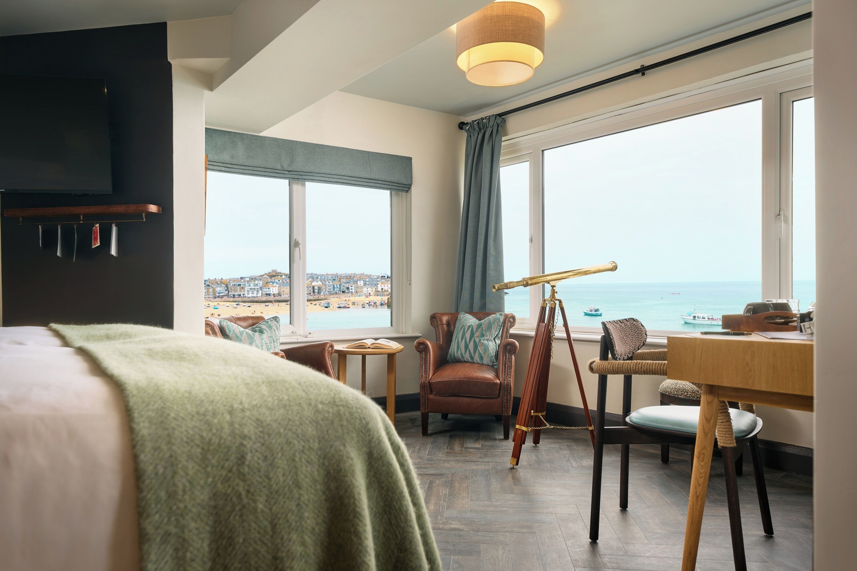 A hotel room with a large window, a telescope, a desk, and a comfortable seating area.