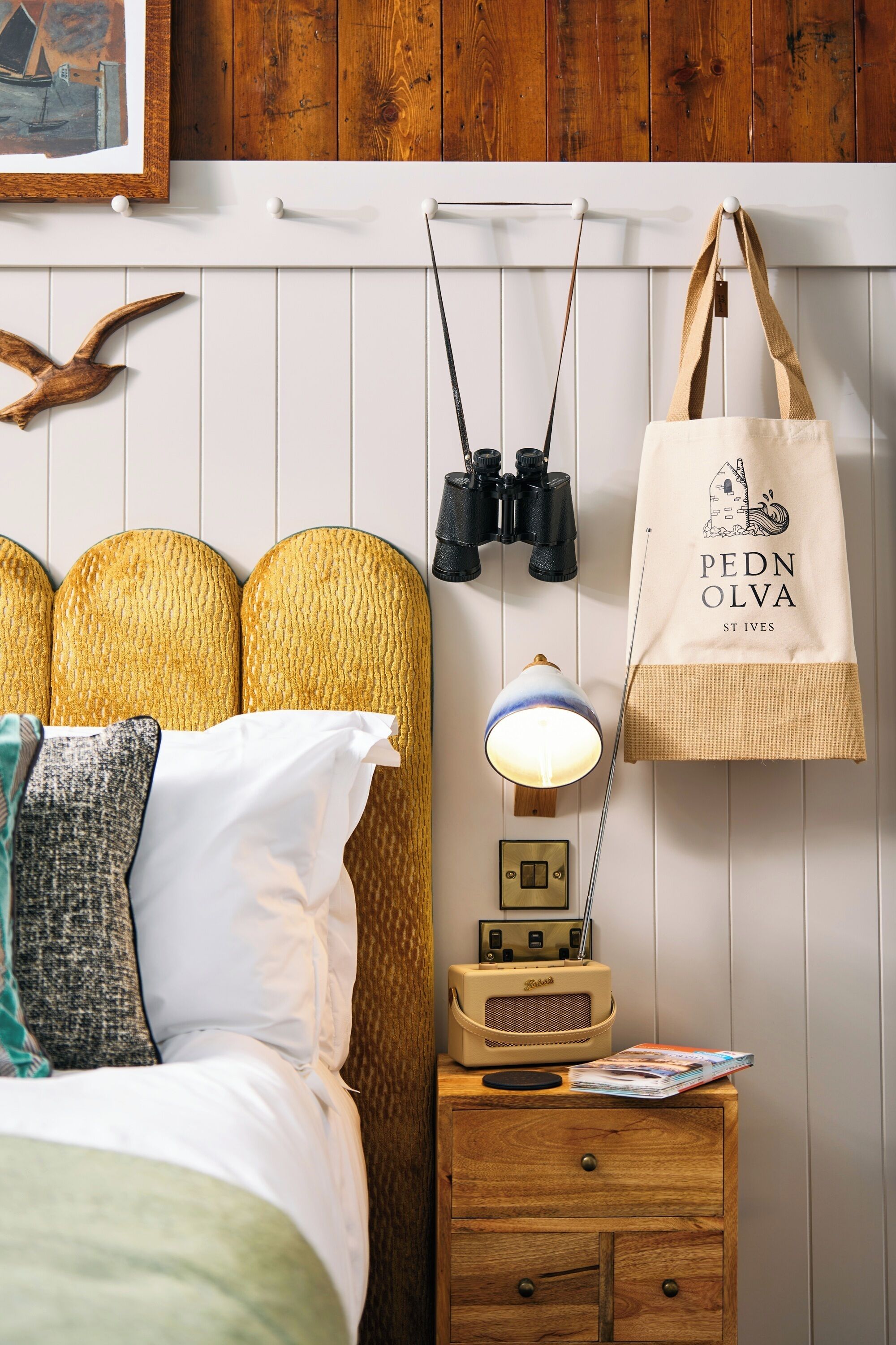 A neatly arranged bedroom with a bed, bedside lamp, radio, and a wall-mounted bag.