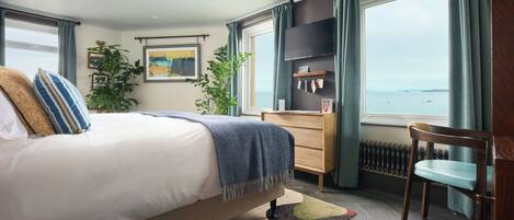 Un dormitorio con cama, cómoda, silla, televisor y vista al mar.
