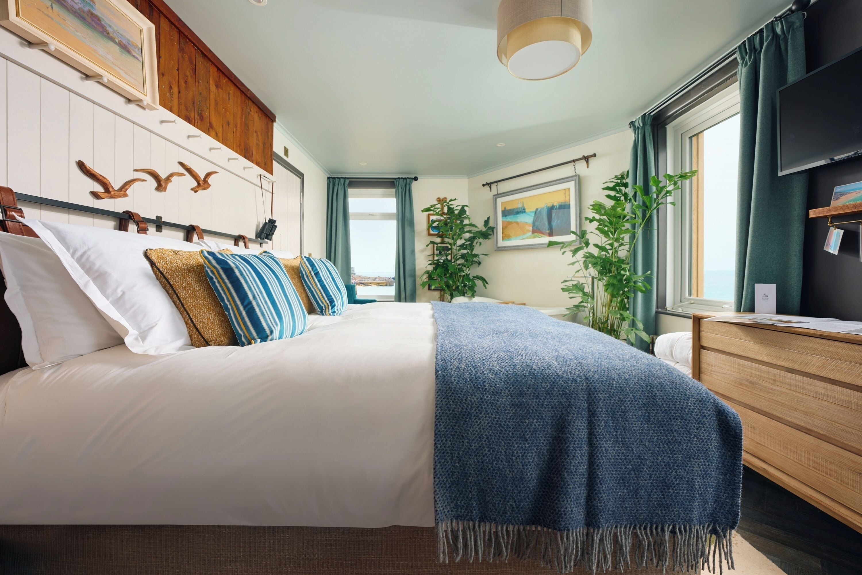 Un dormitorio con una cama grande, un aparador de madera, una ventana con cortinas y un cuadro en la pared.