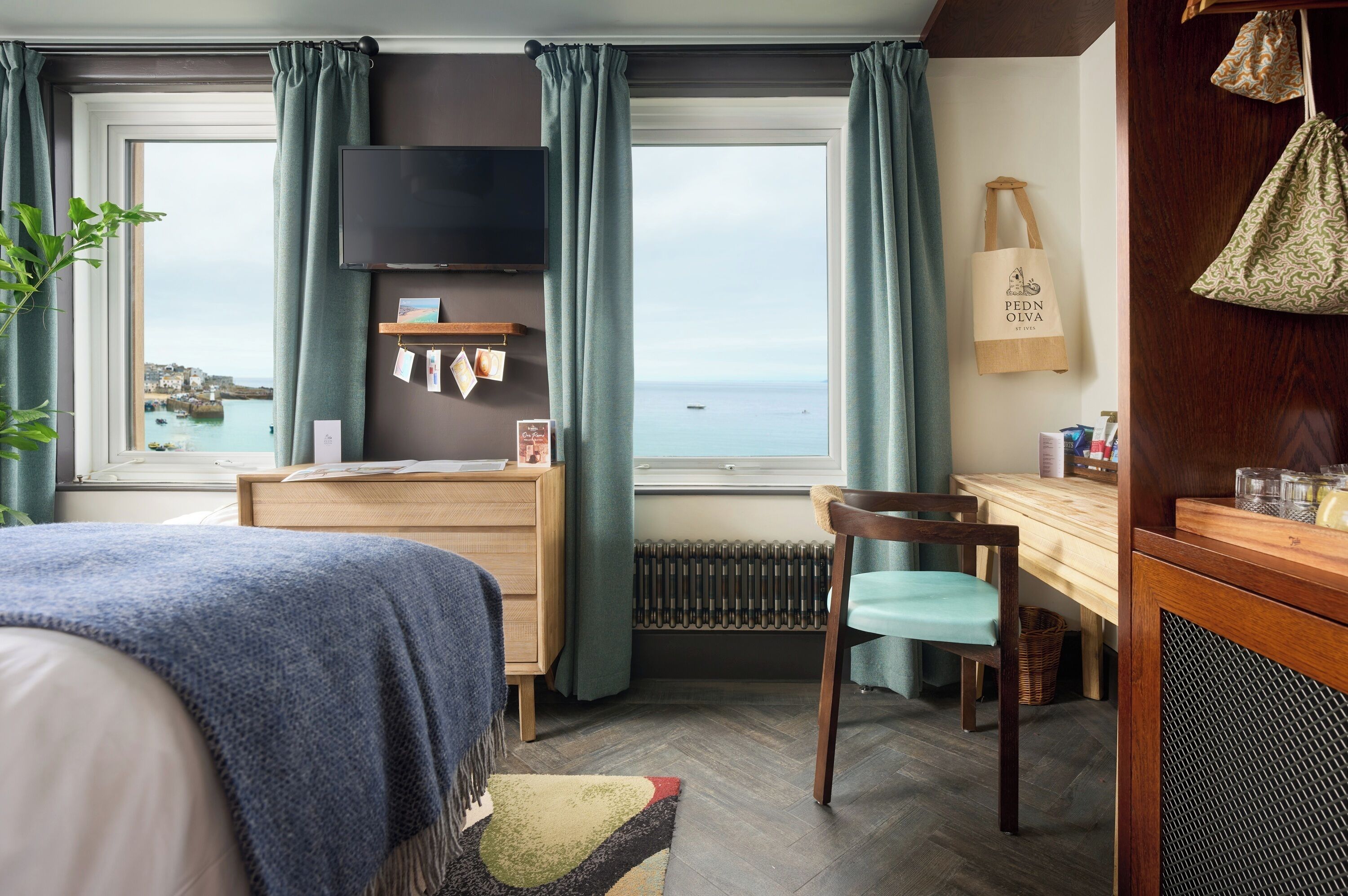 A bedroom with a bed, a desk, a chair, a TV, and a view of the sea.