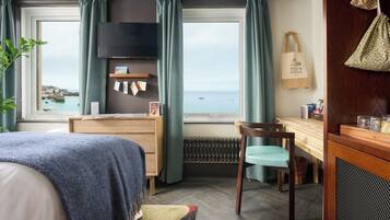 A bedroom with a bed, a desk, a chair, a TV, and a view of the sea.