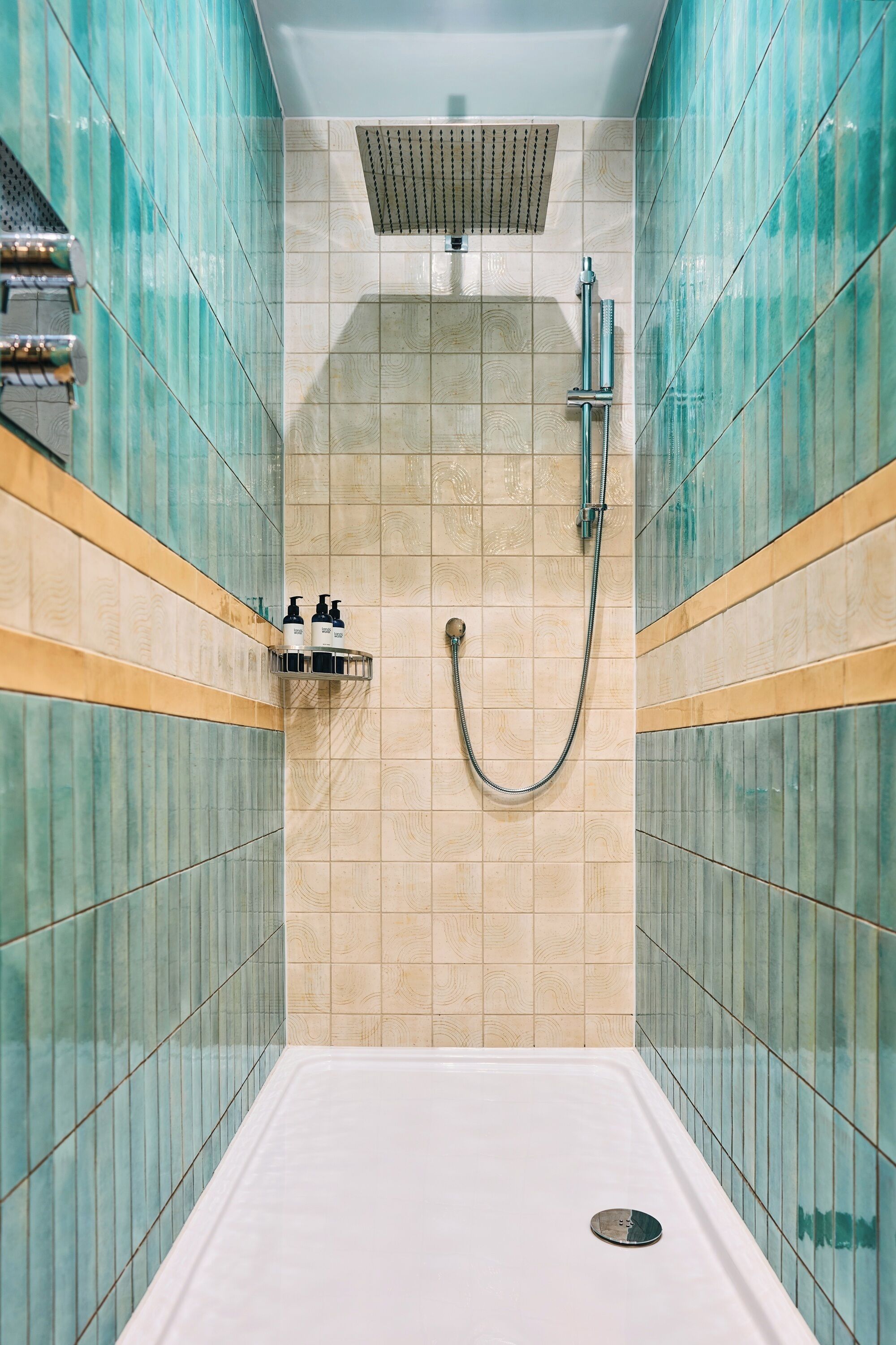 A shower room with a tiled wall, a showerhead, and a handheld shower attachment.