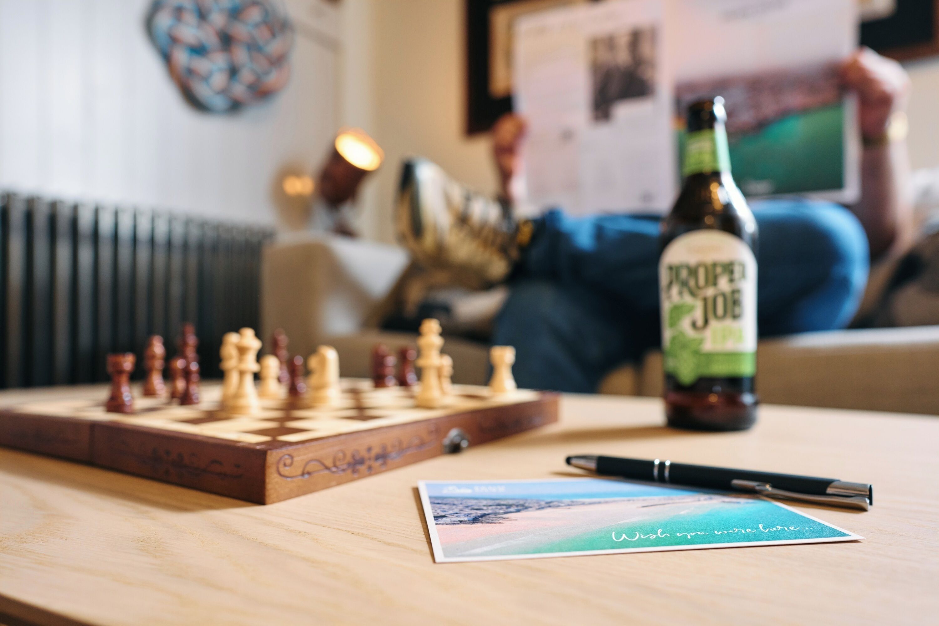 A chessboard, a bottle of beer, a pen, and a postcard on a table.
