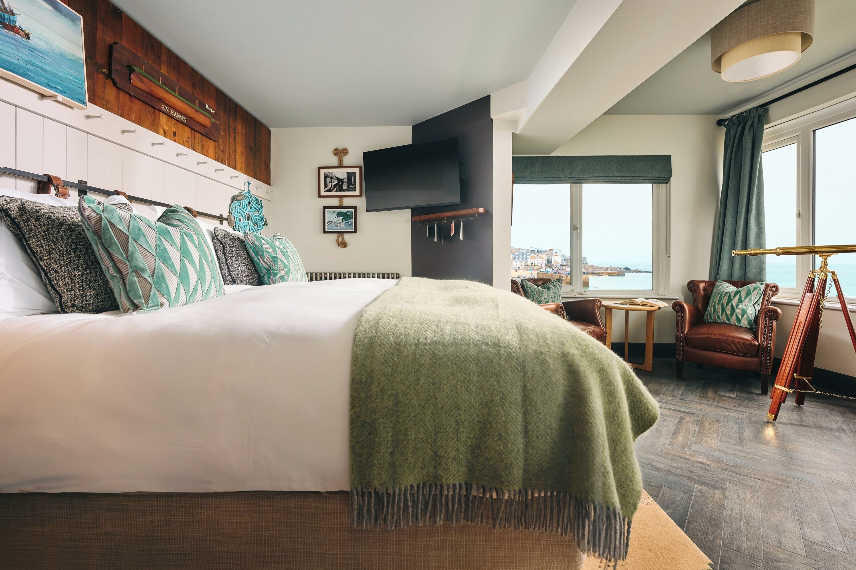 A hotel room with a large bed, a television, a small table, a chair, and a view of the city through the window.