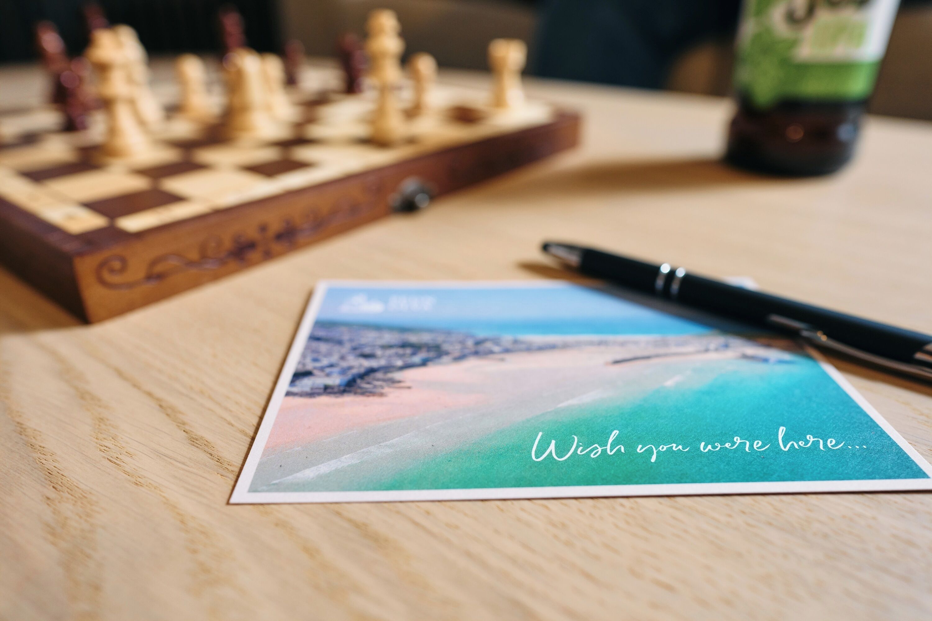 Een schaakbord, een pen en een ansichtkaart met een mooi landschap en een boodschap.