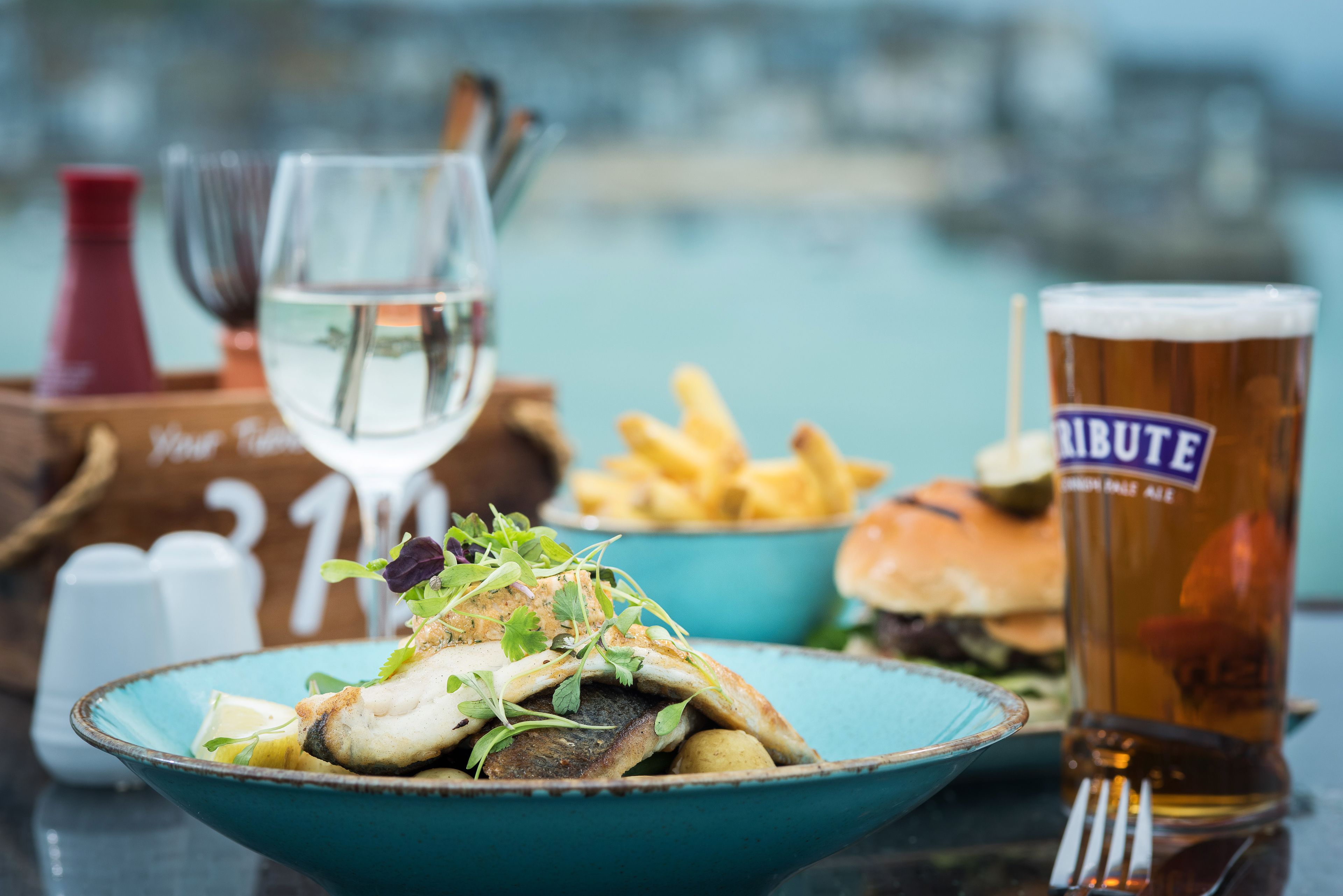 A meal with fish, fries, and a burger, along with a glass of beer and a glass of water.