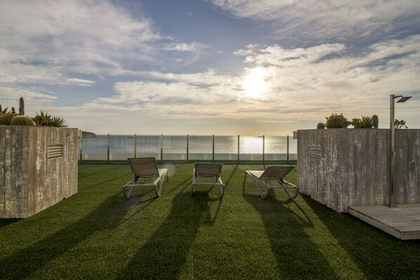 A rooftop terrace with three lounge chairs, a wooden deck, and a view of the ocean.