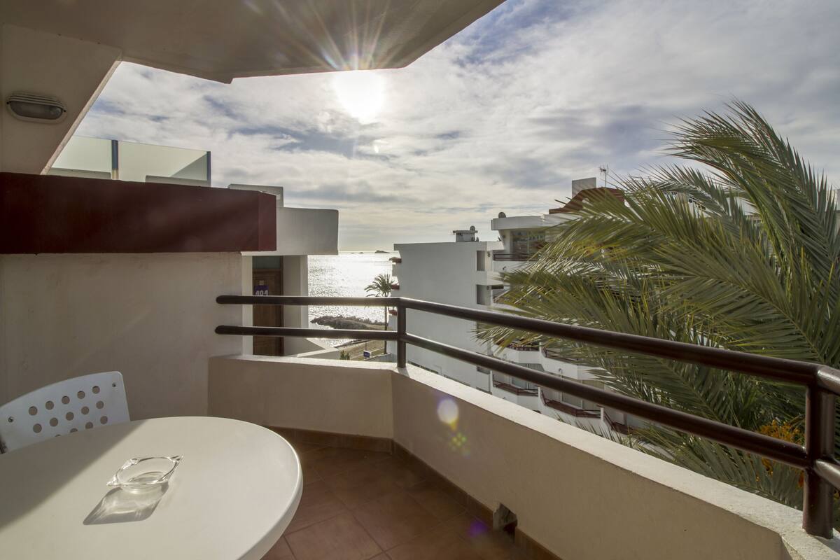A balcony with a view of the sea, a white table, and a chair.