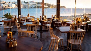 Un área de comedor al aire libre con mesas y sillas de madera, con vistas a la ciudad costera.