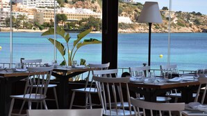 Un restaurante con mesas dispuestas para comer, con vistas al mar y edificios en el fondo.