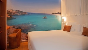 Un dormitorio con una cama grande, una silla y vistas a la costa con barcos.