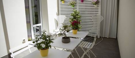 An outdoor patio with white tables and chairs, potted plants, and a white fence with hanging flower pots.