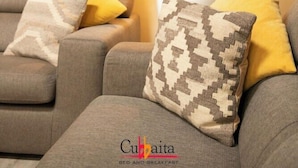 A living room with a grey sofa, yellow and patterned cushions, a large potted plant, and a framed picture on the wall. - B&B Cubbaita (Palermo)