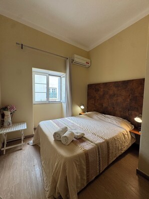 Una cama bien hecha con toallas enrolladas, una lámpara de noche y una ventana con cortinas.
