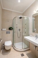 Uma casa de banho moderna com cabine de duche em vidro, lavatório branco e sanita.
