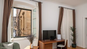 A modern room with a wooden desk, a television, a chair, a sofa, and a window with curtains. - Blasius Residence (Dubrovnik)