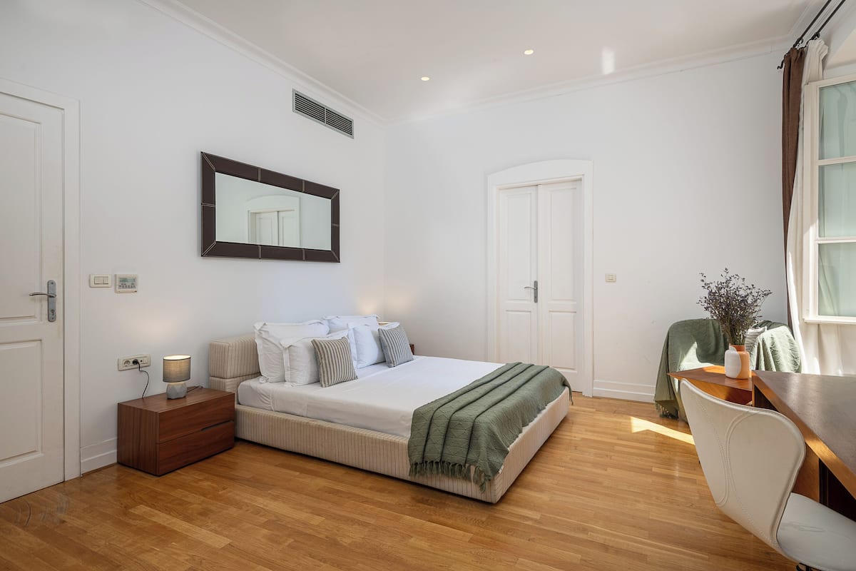 Un dormitorio con cama, mesita de noche, lámpara y espejo en la pared.