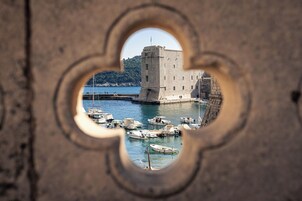 Vista através de uma arcada de pedra de um edifício histórico com uma torre, rodeado por uma marina com vários barcos.