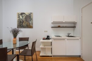 Uma cozinha compacta com armários brancos, uma mesa de jantar de vidro e um quadro na parede.