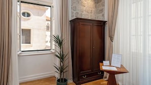 A room with a large window, a wooden cabinet, a potted plant, and a small table with papers. - Blasius Residence (Dubrovnik)