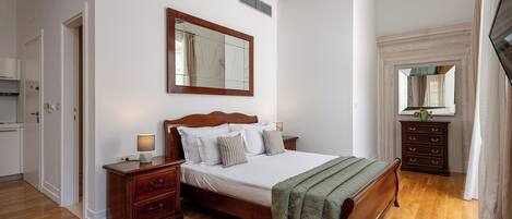 Une chambre à coucher avec un lit en bois, une table de chevet, une commode, un miroir et une fenêtre avec des rideaux.
