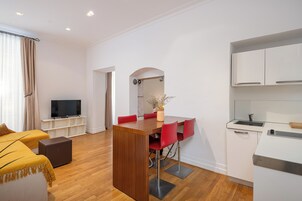 Uma sala de estar moderna com uma mesa de jantar de madeira, cadeiras vermelhas, um sofá e uma televisão.