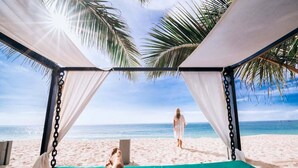 Een strandtent met uitzicht op de oceaan en een persoon die over het zand loopt.