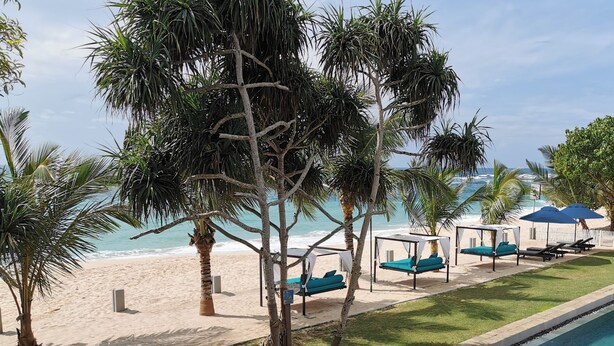 Een zwembadterras met uitzicht op het strand, ligbedden en parasols.