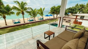 Een balkon met glazen balustrade met uitzicht op een zwembad en strand.