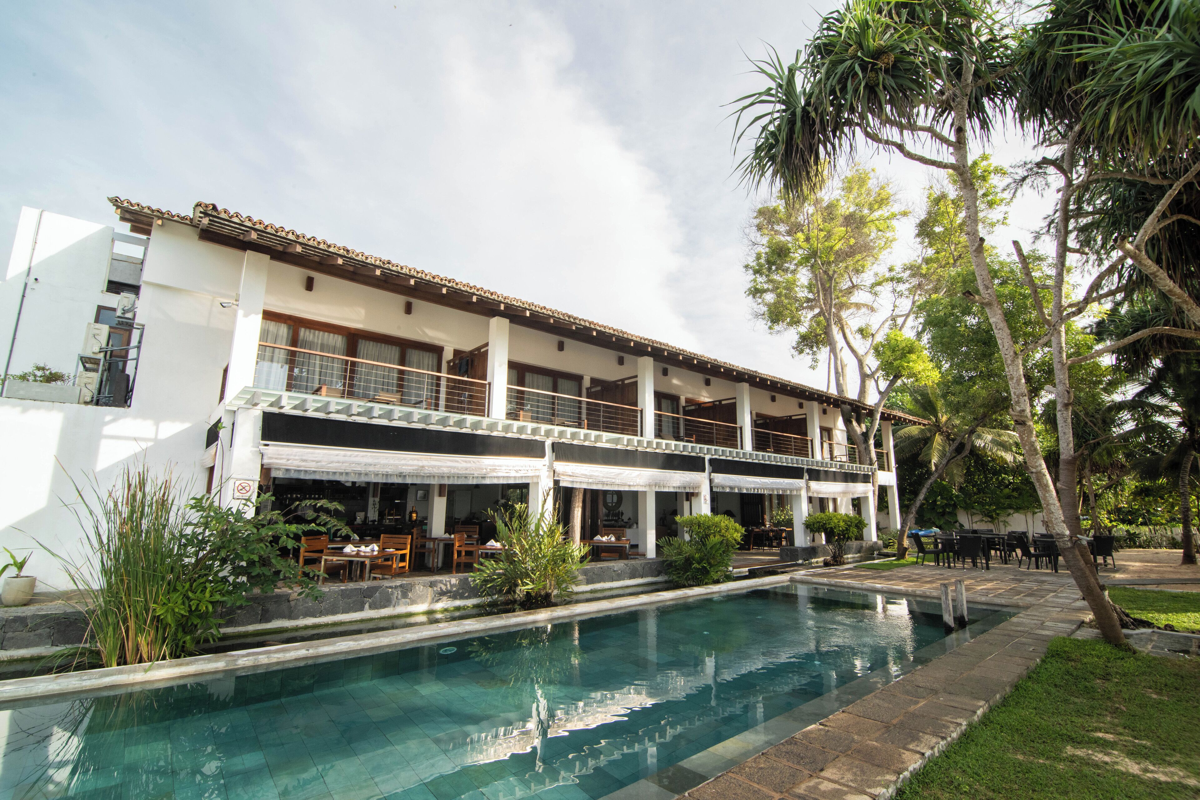 Un edificio de dos pisos con piscina, mobiliario exterior y palmeras.