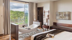 A modern hotel room with a large bathtub, a bed, a seating area, and a view of greenery. - Zen Valley Dalat (Xuan Huong - Da Lat)