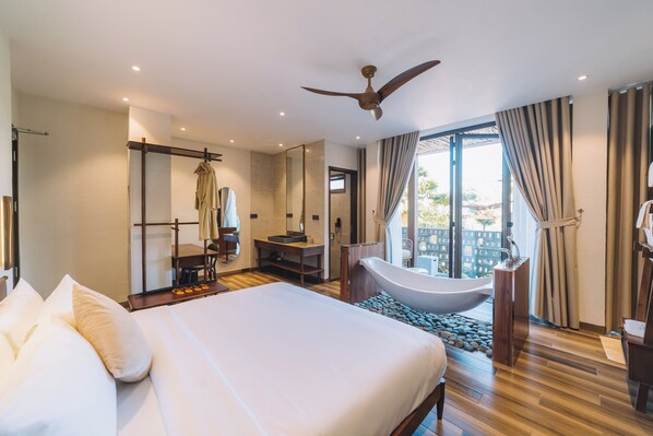 A hotel room with a large bed, a bathtub, a desk with a chair, a mirror, and a ceiling fan.